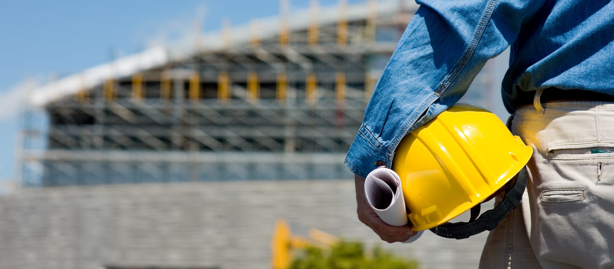 Construction worker holding yellow hard hat and blueprints at building site