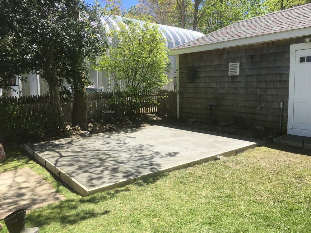 Concrete patio next to gray shingled house with white garage door and green lawn