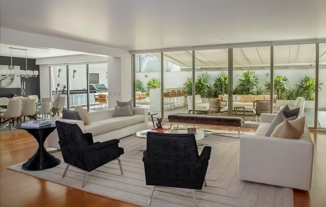 Modern open-concept living room with cream sofas, black chairs, and expansive glass doors opening to terrace