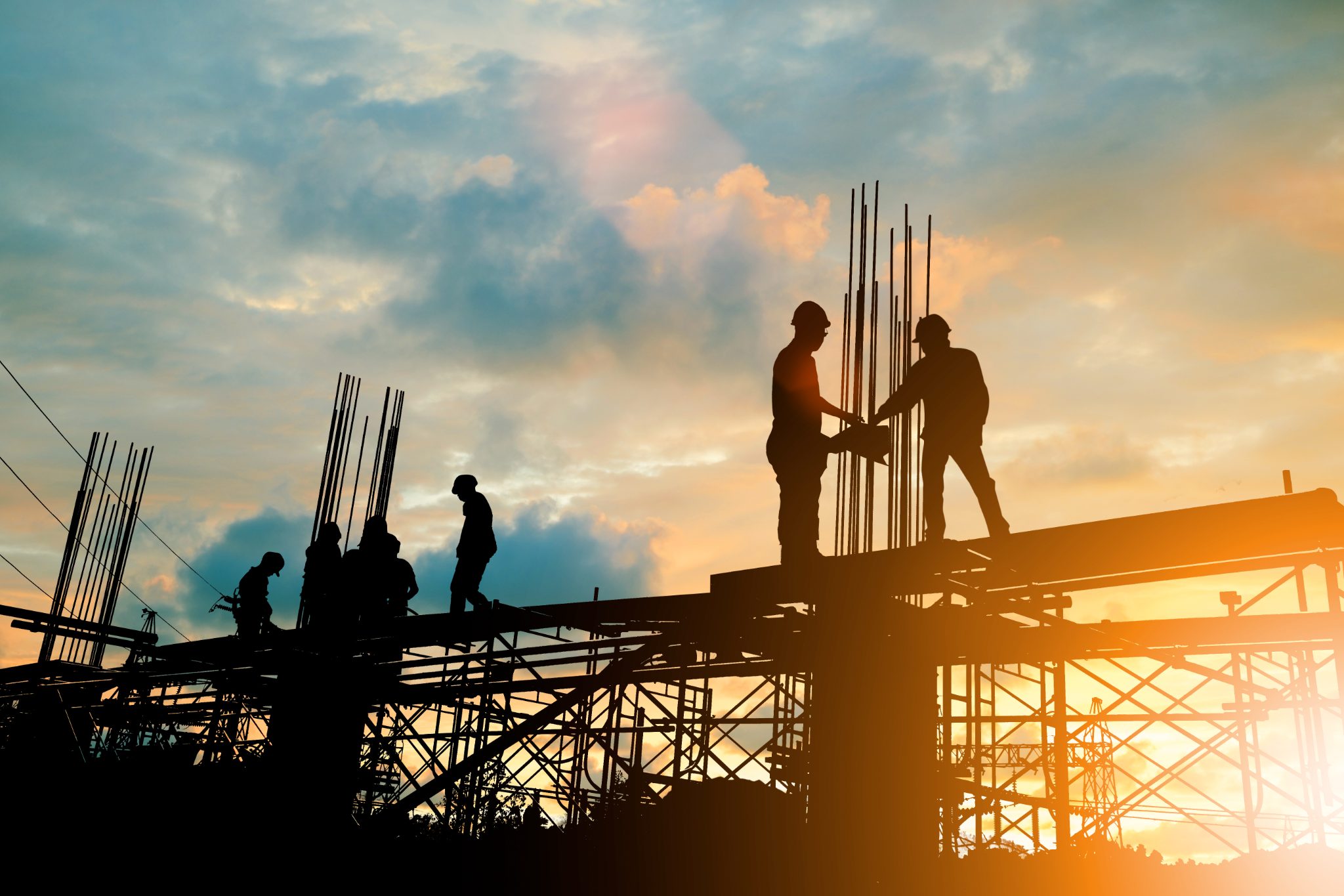 Construction workers on scaffolding at sunset shaking hands