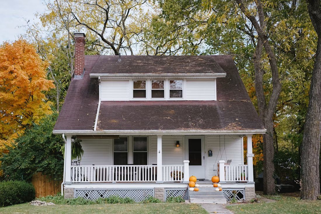 White two-story house with dark roof and brick chimney surrounded by fall foliage