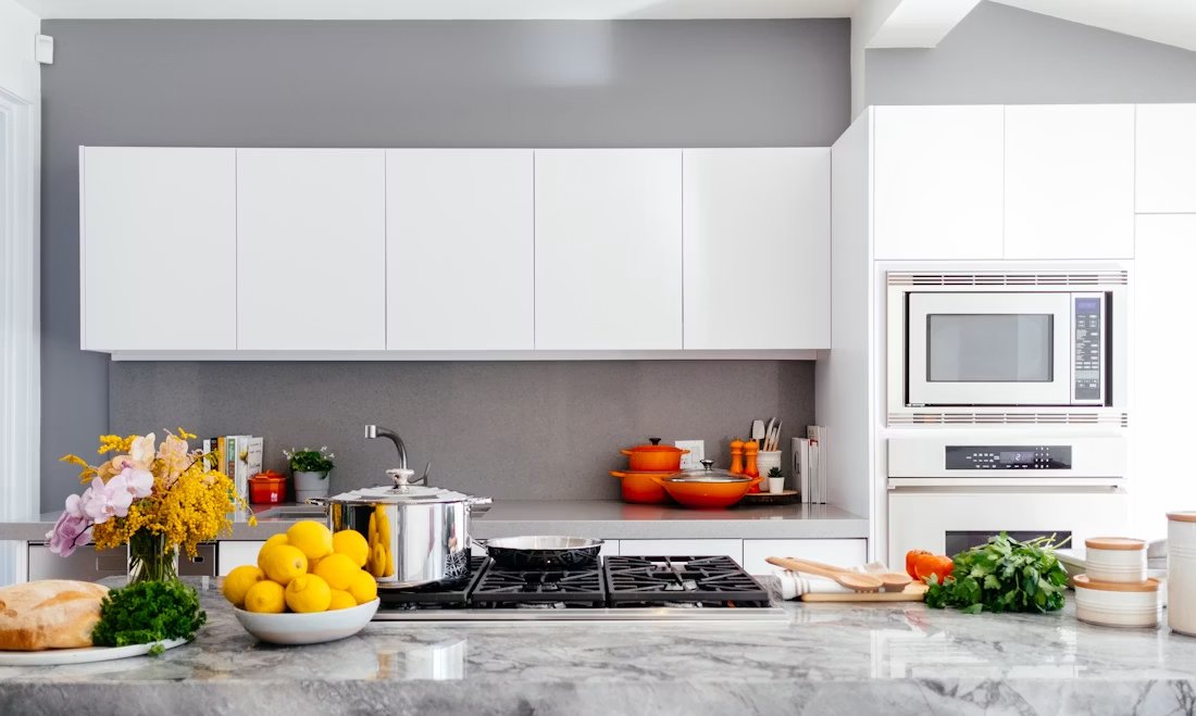 Modern kitchen with white cabinetry, gray backsplash, marble countertop, gas cooktop, and fresh produce