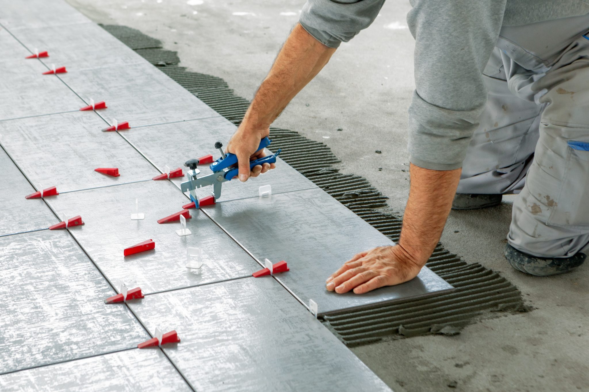 Worker using tile spacer tool with red wedges on concrete floor installation